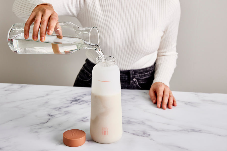 Woman pouring water into a glass milk bottle of freeze-dried vegan milk mix.